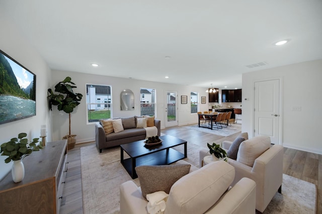 living area featuring light wood-type flooring, visible vents, recessed lighting, baseboards, and a chandelier