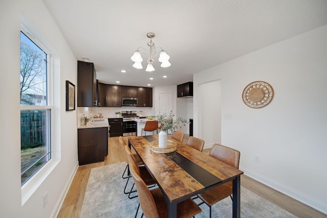 dining area with a notable chandelier, baseboards, light wood-type flooring, and a wealth of natural light