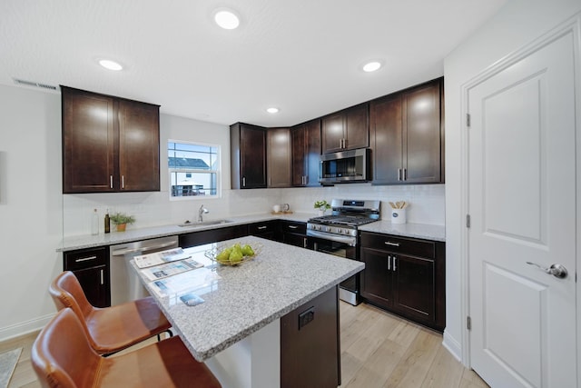 kitchen with dark brown cabinetry, a breakfast bar, light wood-style flooring, appliances with stainless steel finishes, and a sink