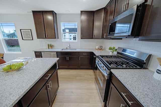 kitchen featuring a sink, dark brown cabinetry, appliances with stainless steel finishes, decorative backsplash, and light stone countertops