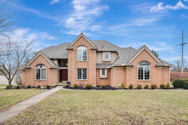 traditional-style house featuring a shingled roof, brick siding, and a front lawn