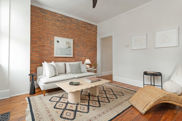 living room with visible vents, baseboards, brick wall, hardwood / wood-style floors, and crown molding