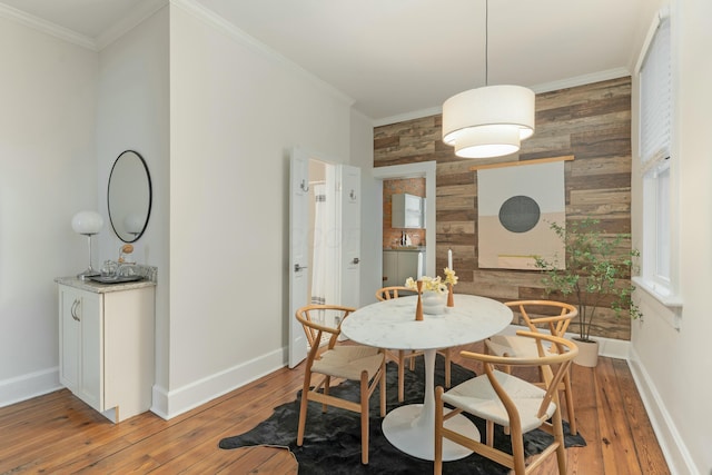 dining room with light wood finished floors, baseboards, an accent wall, crown molding, and wood walls