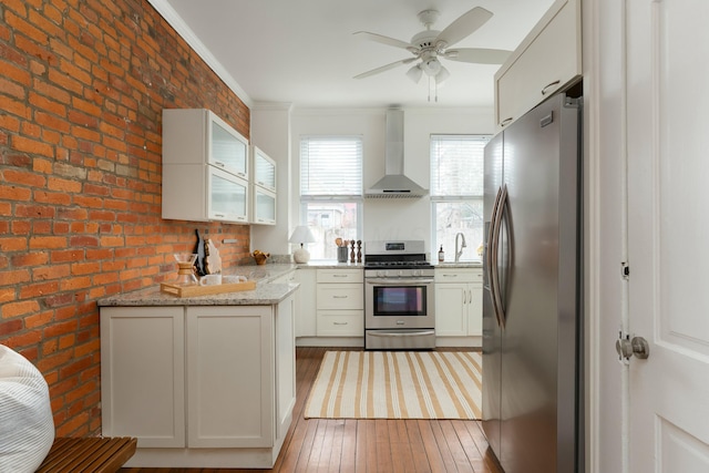 kitchen featuring light wood-style flooring, a sink, appliances with stainless steel finishes, wall chimney exhaust hood, and crown molding