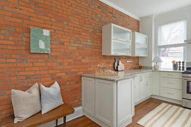 kitchen with light stone counters, brick wall, wood finished floors, glass insert cabinets, and crown molding