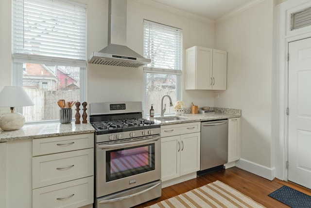 kitchen with wall chimney exhaust hood, ornamental molding, stainless steel appliances, light wood-style floors, and a sink