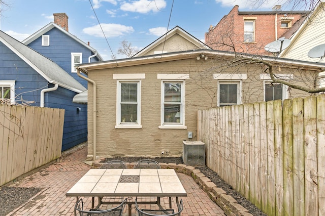 rear view of house featuring cooling unit, a patio area, brick siding, and a fenced backyard