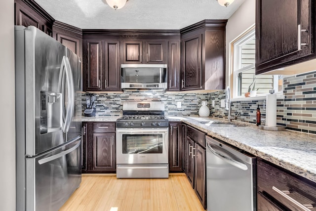 kitchen featuring dark brown cabinets, light wood-style flooring, stainless steel appliances, and a sink