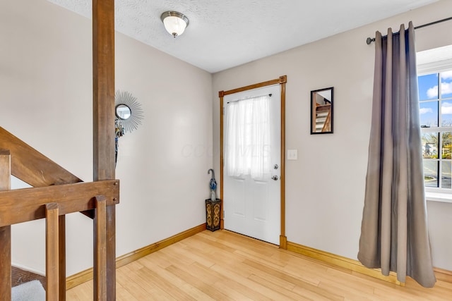 foyer featuring a textured ceiling, light wood-type flooring, and baseboards