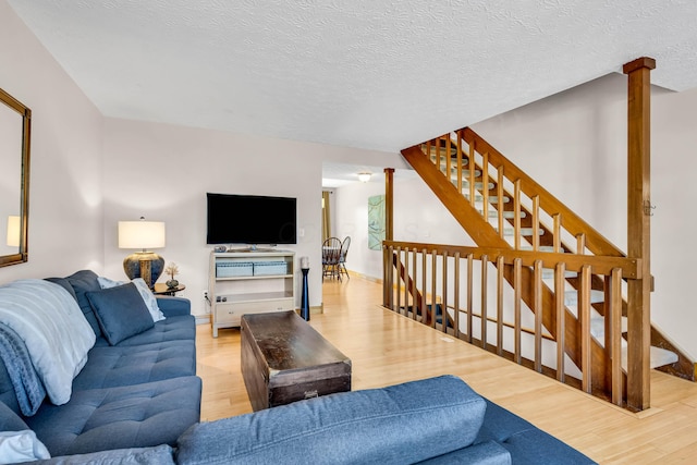 living area featuring stairs, decorative columns, wood finished floors, and a textured ceiling