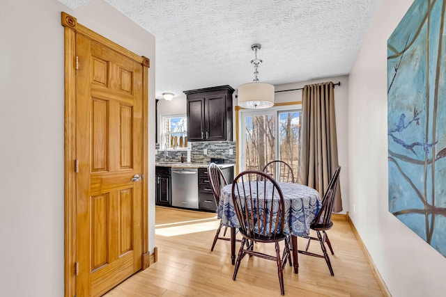 dining area with baseboards, light wood-style floors, and a textured ceiling