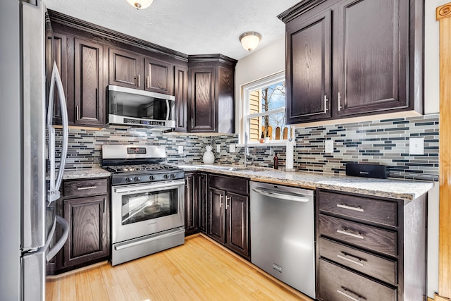 kitchen with light wood-style flooring, a sink, tasteful backsplash, stainless steel appliances, and dark brown cabinets