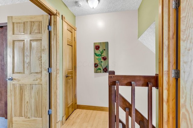 corridor with a barn door, baseboards, light wood-style floors, and a textured ceiling