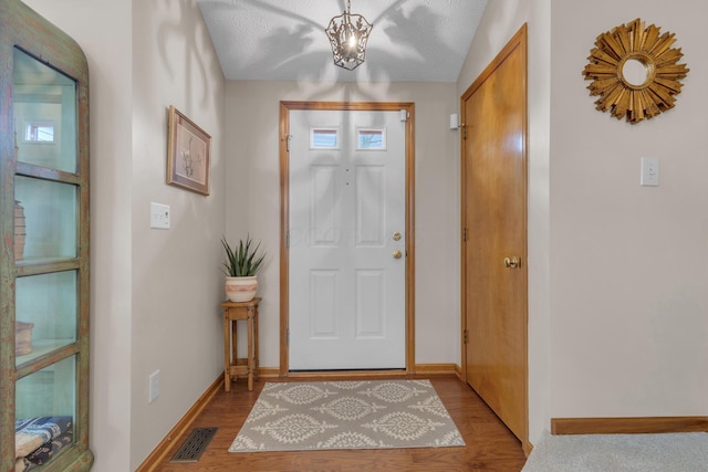 entryway featuring visible vents, a notable chandelier, baseboards, and wood finished floors