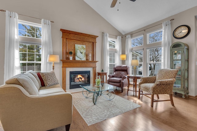 living area featuring a ceiling fan, high vaulted ceiling, wood finished floors, and a tile fireplace