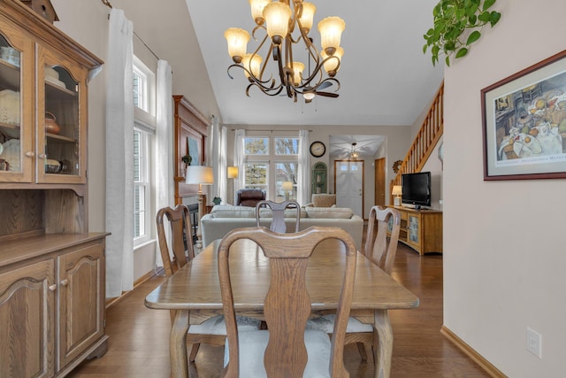 dining room featuring lofted ceiling, baseboards, wood finished floors, and ceiling fan with notable chandelier