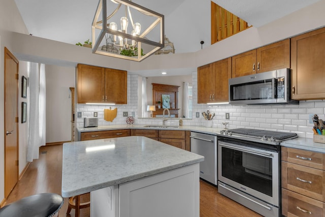 kitchen featuring brown cabinets, a sink, stainless steel appliances, light wood-type flooring, and backsplash