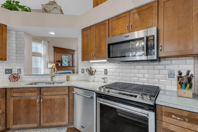 kitchen with stainless steel appliances, a sink, backsplash, brown cabinets, and light stone countertops