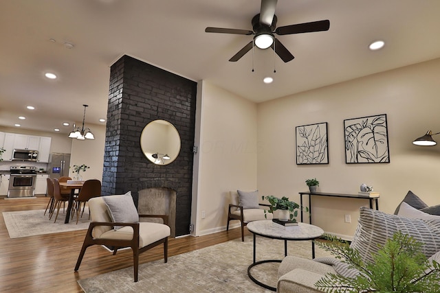 sitting room with recessed lighting, baseboards, light wood-style floors, a fireplace, and ceiling fan with notable chandelier