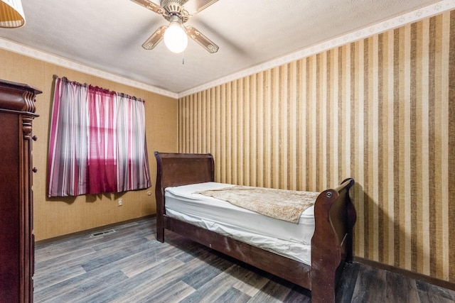 bedroom featuring visible vents, ceiling fan, wood finished floors, baseboards, and wallpapered walls