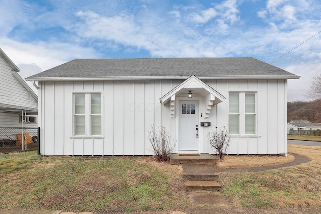 bungalow-style home with roof with shingles, a front lawn, board and batten siding, and fence