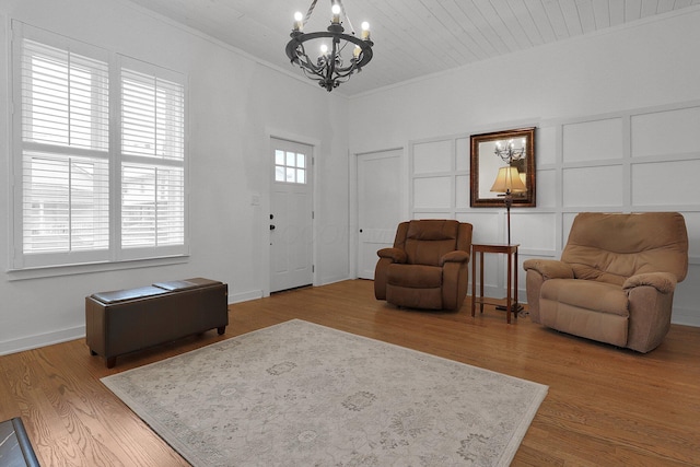 living area with a decorative wall, crown molding, wood finished floors, baseboards, and an inviting chandelier