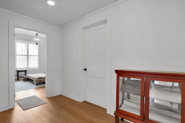 hall with crown molding, an inviting chandelier, wood finished floors, and baseboards