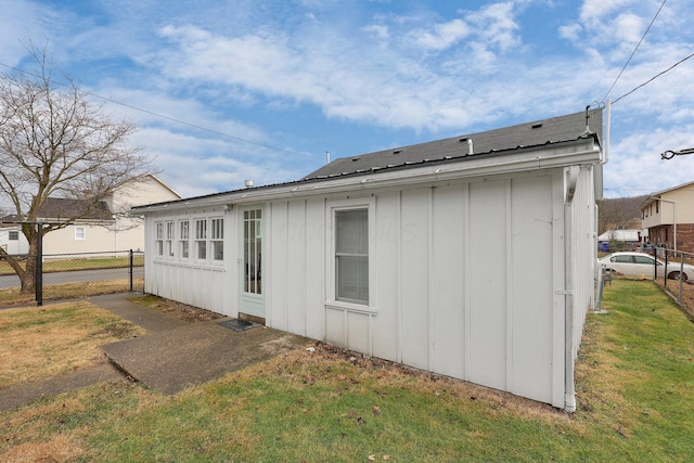 rear view of property with board and batten siding, fence, and a lawn