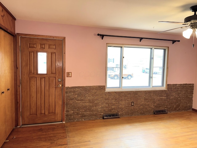 foyer with visible vents, brick wall, a ceiling fan, and wood finished floors