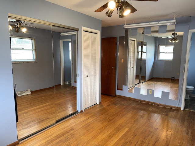 unfurnished bedroom featuring two closets, multiple windows, visible vents, and wood-type flooring