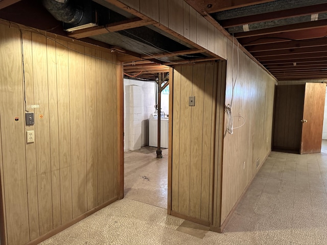 hall featuring washer and clothes dryer, wooden walls, and light floors