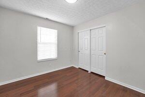 unfurnished bedroom with a closet, a textured ceiling, baseboards, and wood finished floors