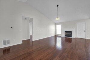 unfurnished living room featuring a fireplace, wood finished floors, visible vents, and high vaulted ceiling