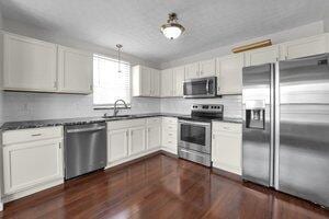 kitchen featuring a sink, tasteful backsplash, dark wood-style floors, white cabinetry, and stainless steel appliances