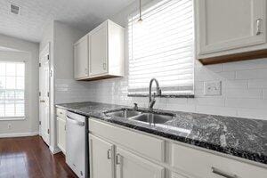 kitchen featuring a sink, backsplash, dark wood-type flooring, and dishwasher