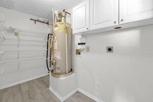 laundry room featuring electric dryer hookup, wood finished floors, gas water heater, cabinet space, and baseboards