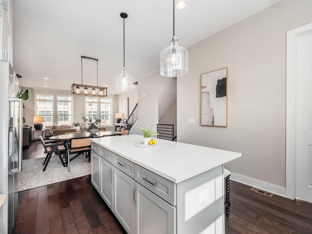 kitchen with a center island, open floor plan, pendant lighting, light countertops, and dark wood-style floors