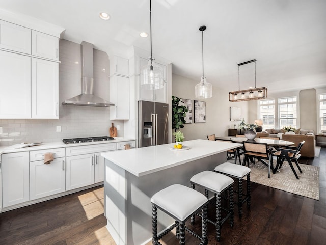 kitchen featuring a kitchen bar, backsplash, gas stovetop, high quality fridge, and wall chimney exhaust hood