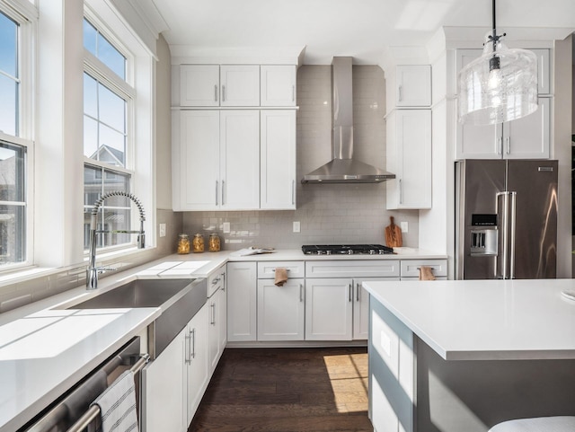 kitchen featuring a sink, stainless steel appliances, light countertops, wall chimney exhaust hood, and tasteful backsplash