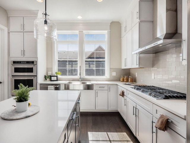 kitchen featuring a sink, appliances with stainless steel finishes, light countertops, and wall chimney range hood