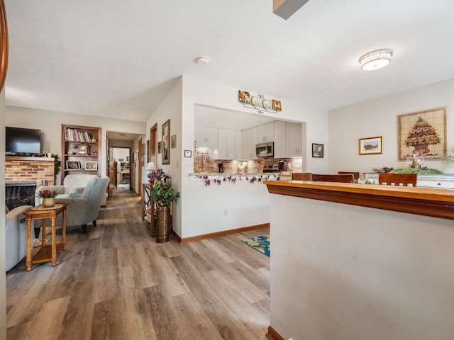 kitchen featuring a fireplace, light countertops, stainless steel microwave, white cabinetry, and light wood-type flooring