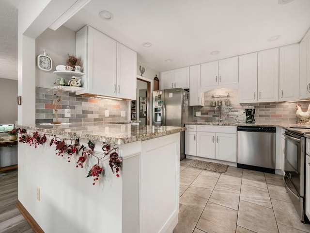 kitchen featuring light stone counters, stainless steel appliances, a sink, white cabinets, and open shelves