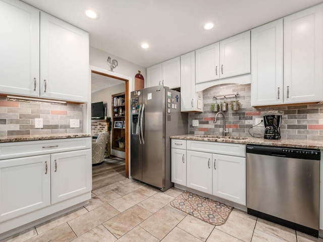 kitchen featuring stainless steel appliances, a sink, light stone countertops, and white cabinets