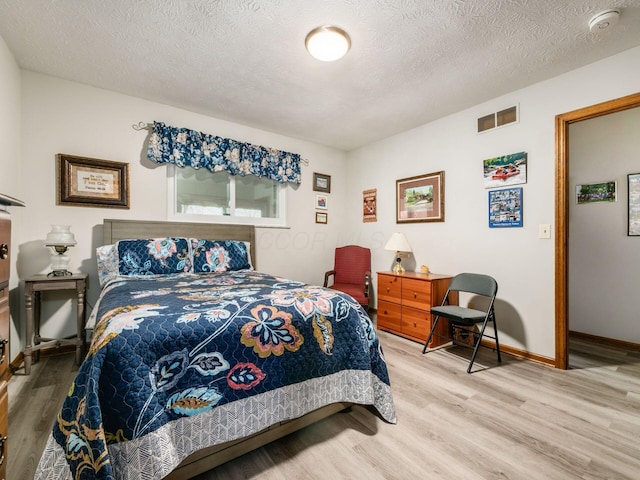 bedroom featuring baseboards, a textured ceiling, visible vents, and wood finished floors