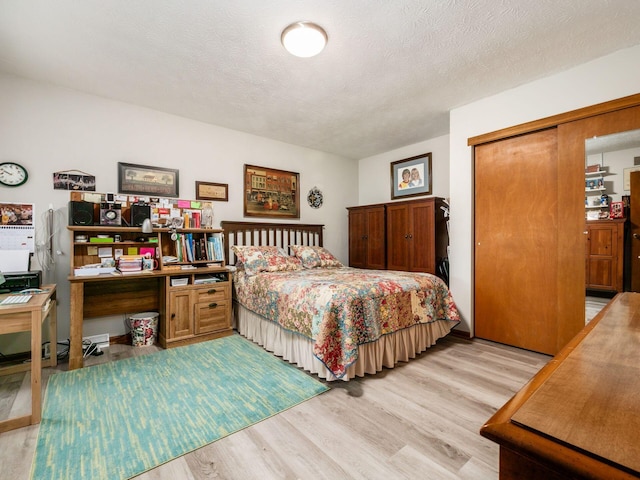 bedroom with a textured ceiling, light wood finished floors, and a closet