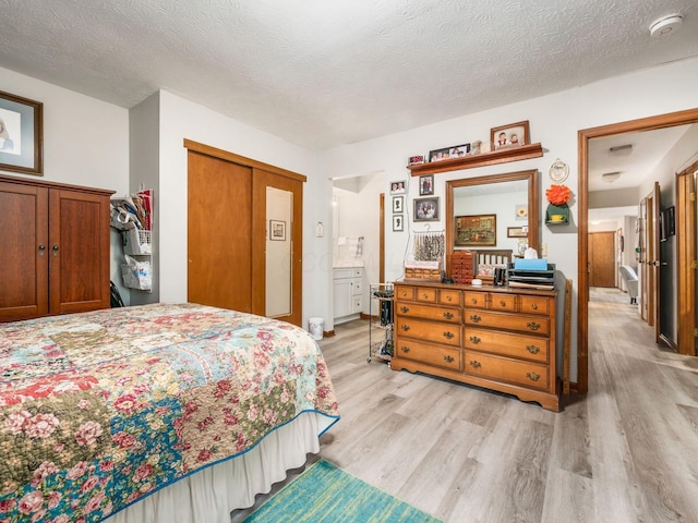 bedroom featuring light wood-type flooring, a closet, a textured ceiling, and ensuite bathroom