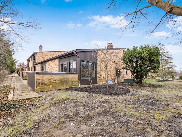 exterior space with brick siding, a chimney, and central AC unit