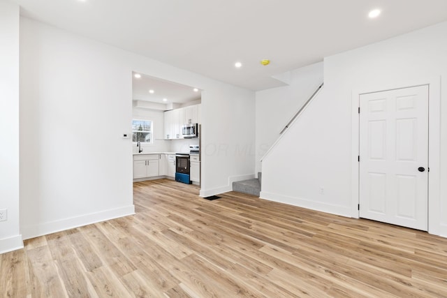 unfurnished living room with stairs, baseboards, light wood-style flooring, and recessed lighting