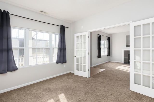 carpeted empty room featuring visible vents, baseboards, a tiled fireplace, and french doors