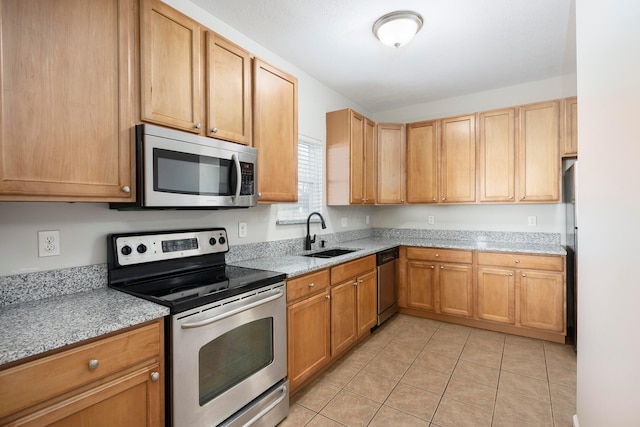 kitchen featuring light tile patterned floors, appliances with stainless steel finishes, light stone counters, and a sink